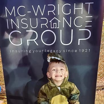 Child in costume in front of Mc-Wright Insurance Group banner at Halloween event