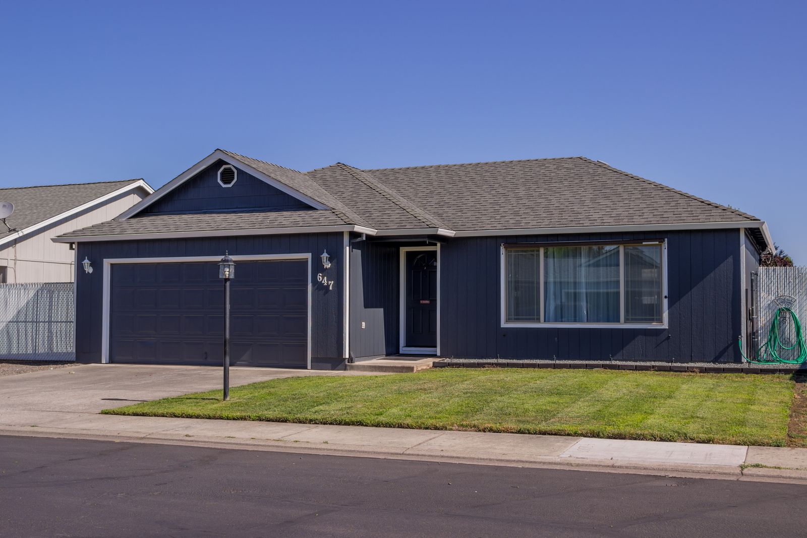 A navy blue single-story house with a gray shingle roof, attached two-car garage and freshly mowed front lawn, seen from the street