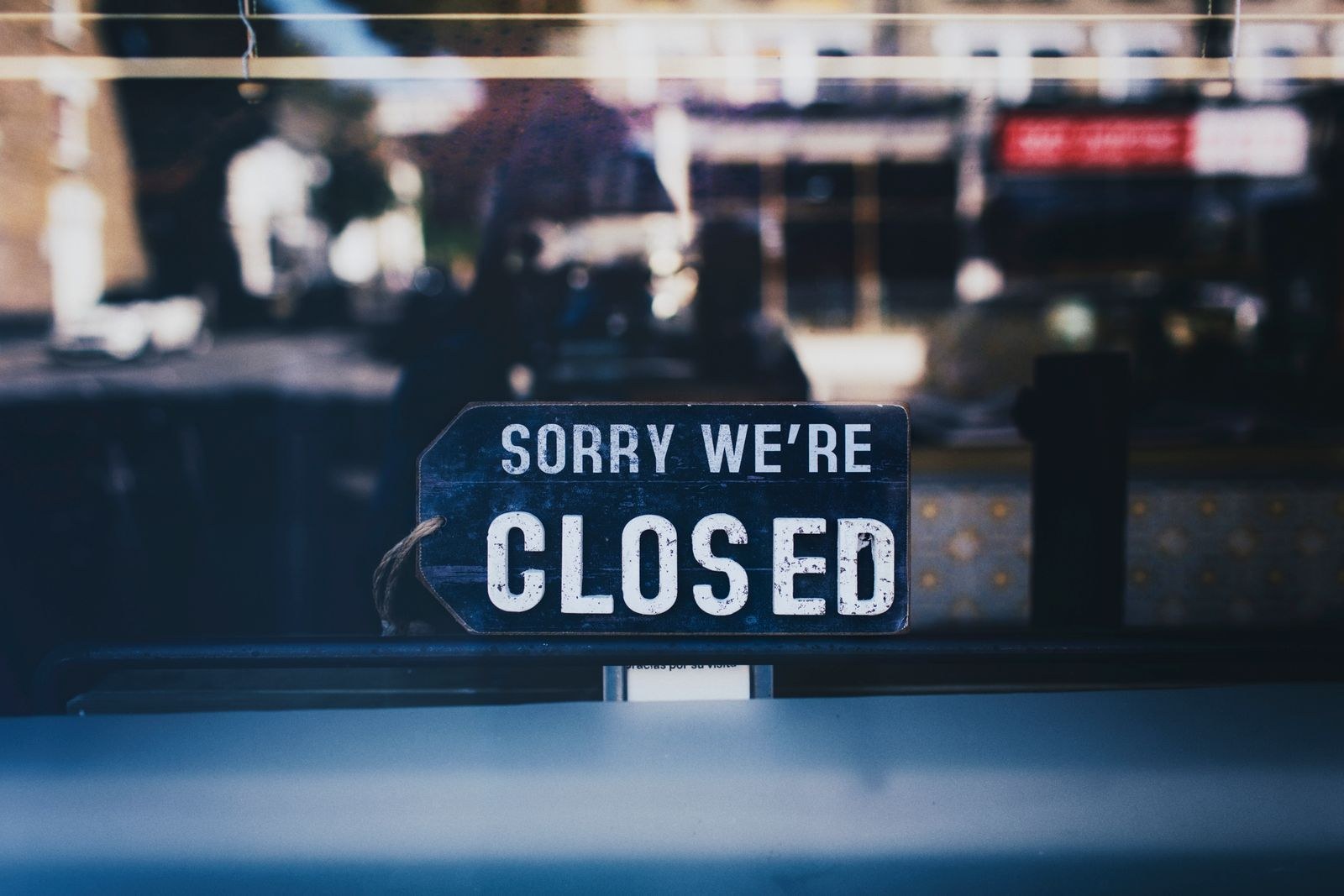 A Sorry We're Closed sign hanging inside a shop's glass window, with the street blurred in reflection