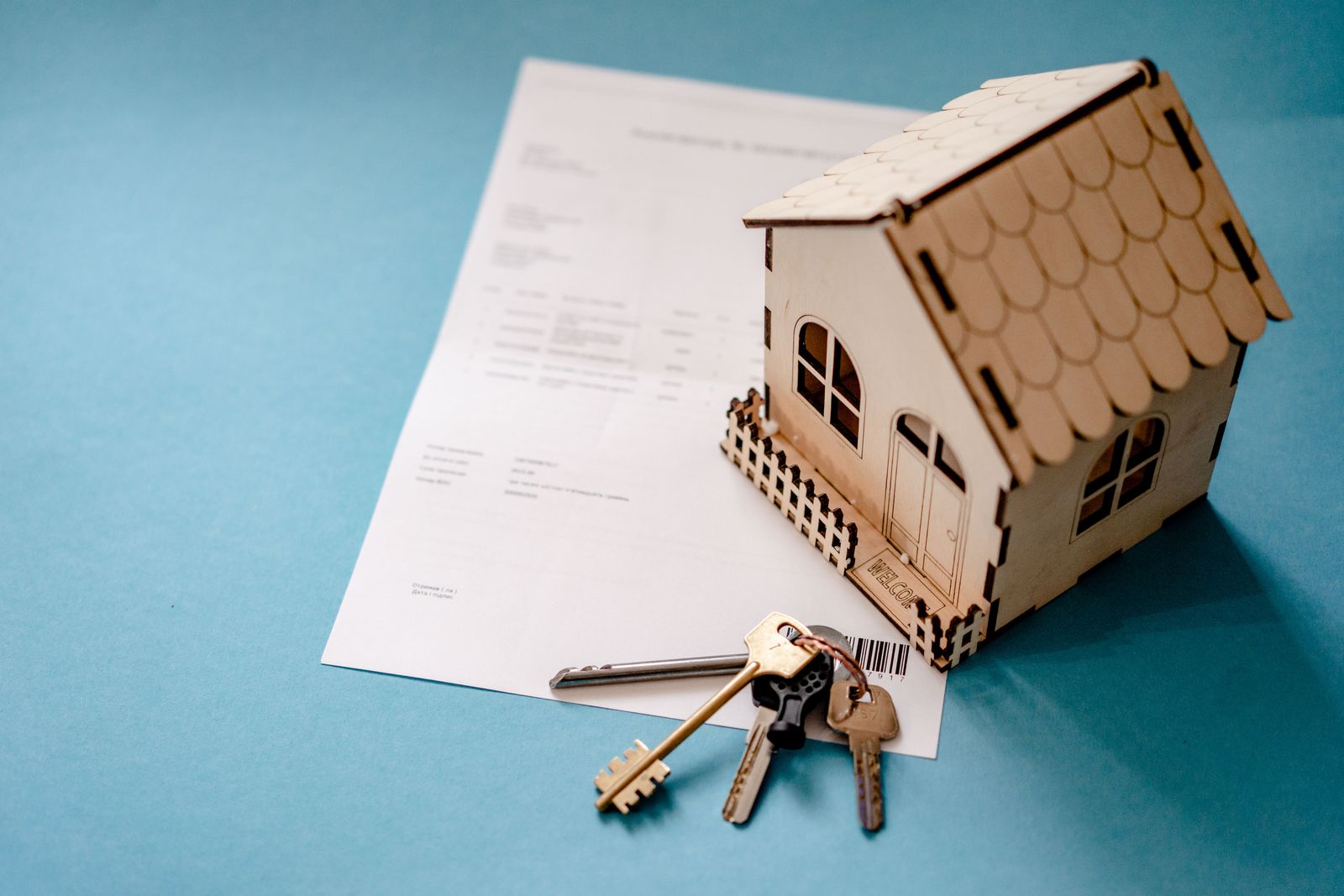 House keys and a contract on a table in front of a wooden house model