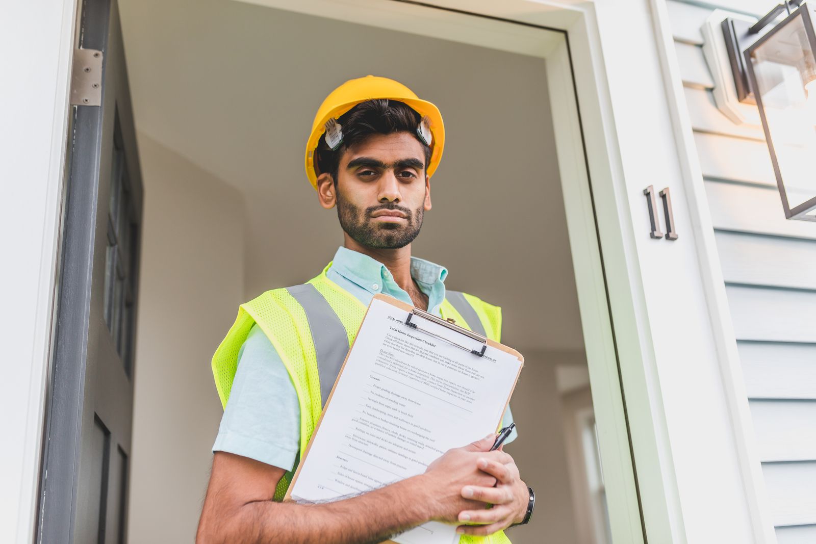 A contractor in a hard hat holding a clipboard of paperwork at a doorway