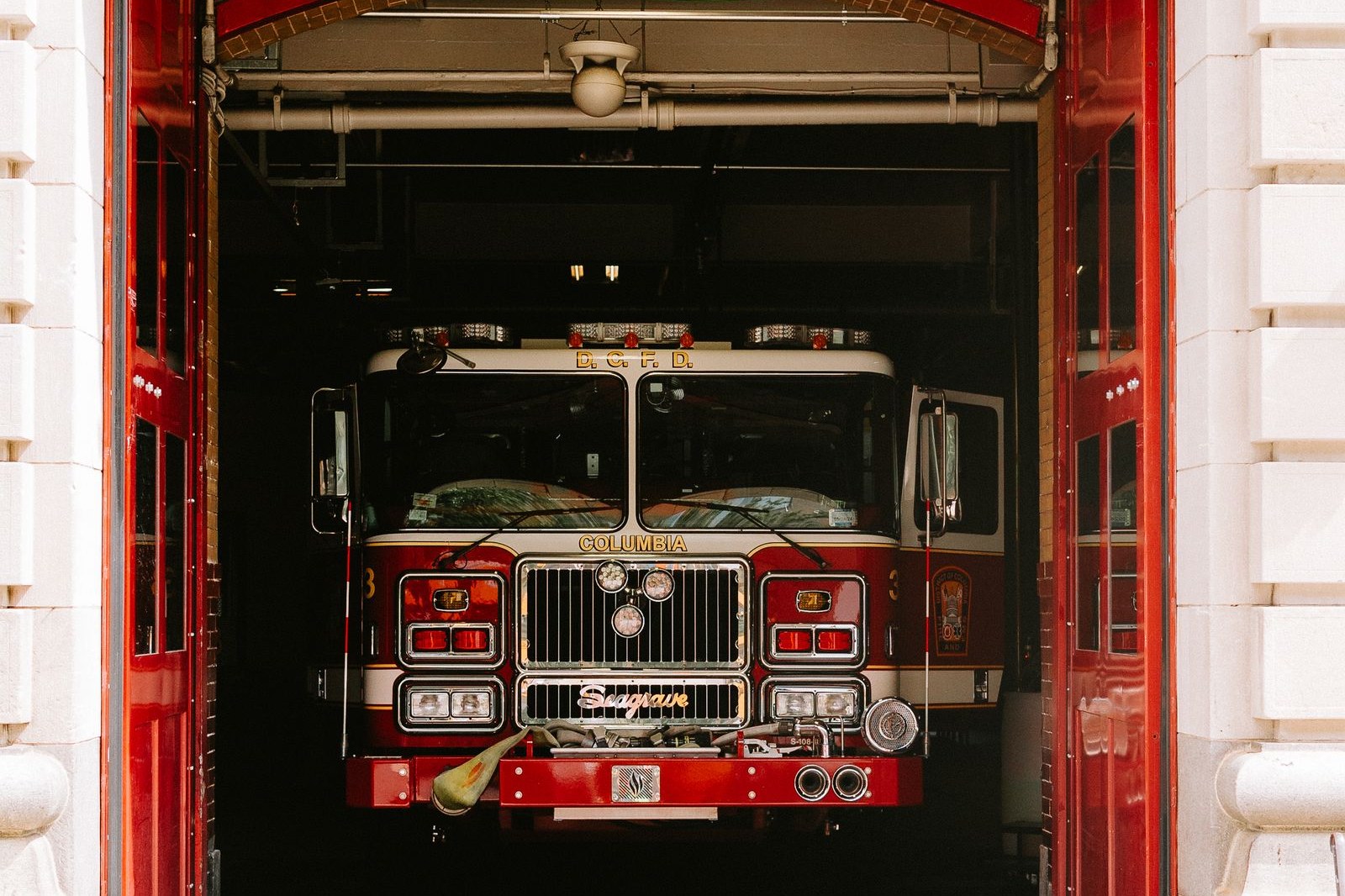 A red fire engine parked inside a fire station bay, seen through the station's open red doors
