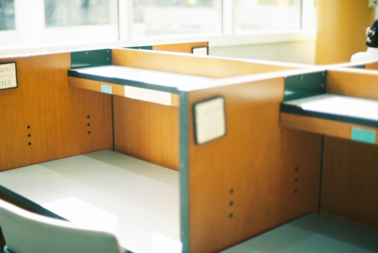 An empty wooden office cubicle with a bare desktop and a chair pushed in, lit by daylight from a window