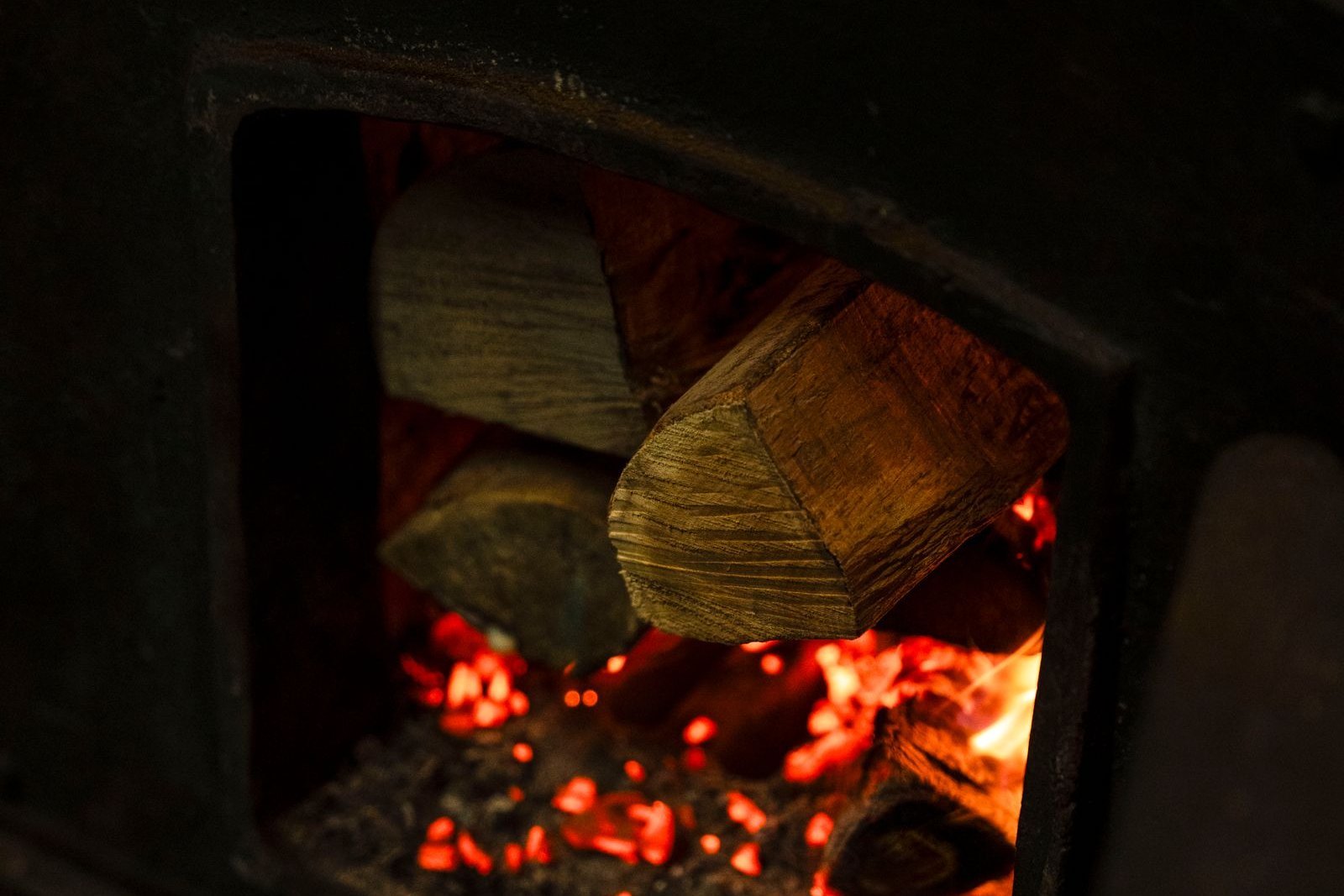 Split logs burning down to glowing red coals inside the open cast-iron firebox of a wood stove