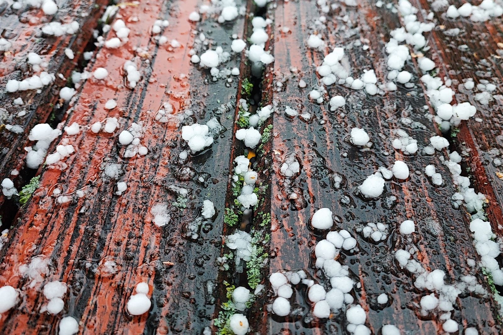 Small white hailstones scattered across wet reddish wooden deck boards after a storm