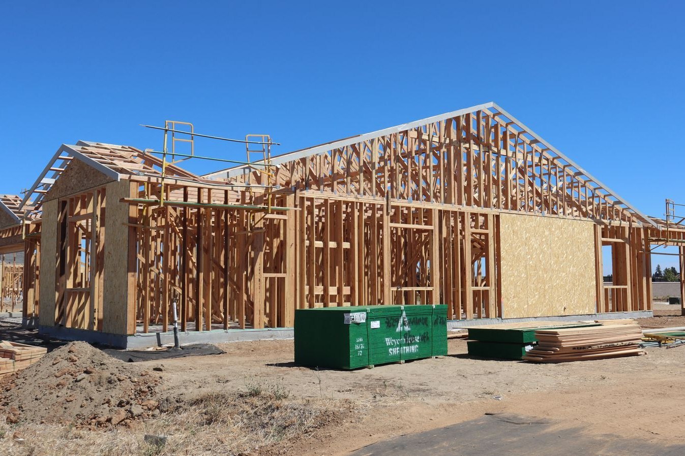 Wooden house framing under construction in bright sunlight, with open stud walls and no exterior cladding yet