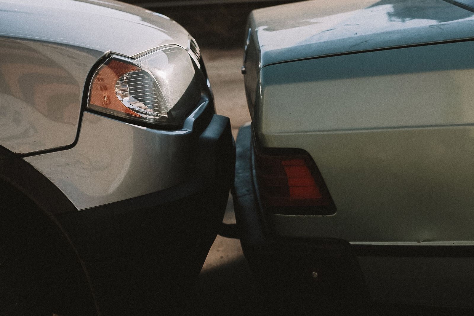 The front bumper of a silver car pressed against the rear corner of a pale green sedan in a minor collision